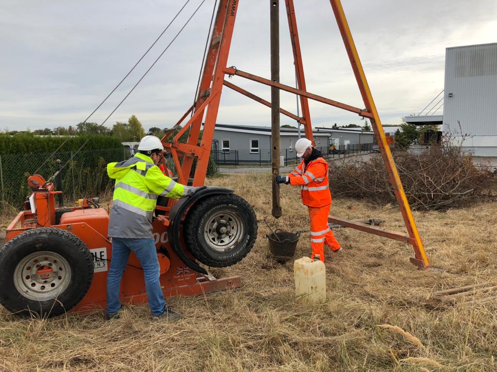 Geotechnical survey in Malaysia conducted by Altus Oil & Gas team using drilling equipment in a field site. Two workers in safety gear are operating machinery for soil sampling and analysis.