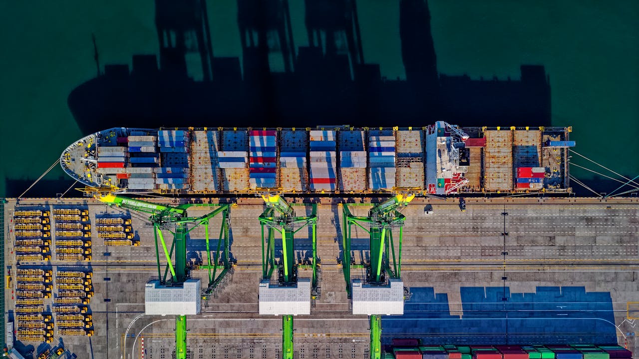 Aerial view of a container ship docked at a Malaysian port, with cranes loading and unloading cargo, representing the operations managed by cargo agents in Malaysia for efficient logistics and freight handling.