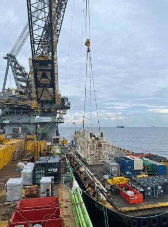 Large crane vessel performing loading operation, with stinger structure being loaded onto an offshore construction vessel to conduct pipeline installation project.